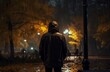 Man in raincoat walks through park at night, illuminated by burning lights Autumn rain falls