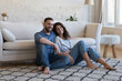 © fizkes - Happy attractive young adult husband and wife resting on heating clean carpeted floor, sitting close, looking at camera, smiling, laughing. Married couple of new homeowners in love home portrait