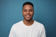 © Delta Amphule - Everyday people. A smiling handsome African American man. Wearing a white t-shirt. On a blue background. Friendly man. Down-to-earth and approachable. Portrait.