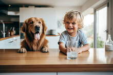Cheerful Little Boy Is Posing With A Golden Retriever Dog At The Kitchen Table. Funny Kid And His Pet Preparing For Breakfast At Home. Happy Smiling Boy And Puppy Enjoy Their Time Spent Together.
