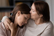 © fizkes - 60s mom hugs and kisses on forehead adult daughter seated on couch at home close up. Parent comforting protecting grown up child, showing love provide moral support during heart-to-heart talk concept