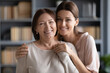 © fizkes - Head shot different generation relatives women standing in living room looking at camera, adult daughter hugs old mother, concept of love, protection, warm relations between grown up child and parent
