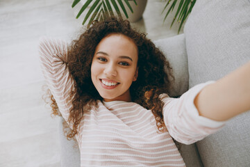 Wall Mural - Close up young woman wear casual clothes lay down on grey sofa couch do selfie shot pov mobile cell phone stay at home hotel flat rest relax spend free spare time in living room indoor Lounge concept