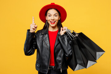 Wall Mural - Young insighted woman wear casual clothes red hat hold shopping paper package bags holding index finger up with great new idea isolated on plain yellow background. Black Friday sale buy day concept.