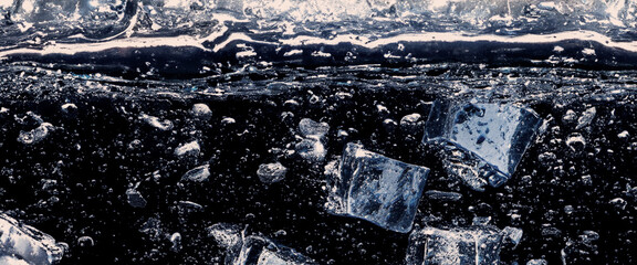 Wall Mural - Water splashing and ice cube. Ice splashing into a glass of water. Underwater pouring ice cubes falling into clear watering background. Refreshing chill drinking. Ices in a glass with blue background