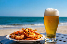 A glass of beer and a portion of fried prawns on a table at the beach