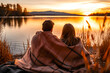 A couple wrapped in a warm blanket and sitting by a lake, enjoying a nice sunset