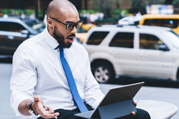 Wall Mural - Black surprised entrepreneur looking at tablet screen outside