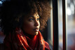 Portrait of a pretty calm African American woman with curly afro hair and wearing a red scarf standing indoors and looking out window