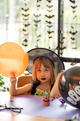 Wall Mural - A cute gir is sitting at a table with a balloon at a master class on crafts for Halloween. 