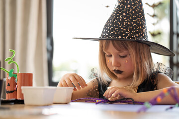 Wall Mural - Children's Halloween party. A girl in a witch costume makes crafts for decorating a house on Halloween