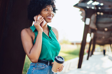 Happy young female with coffee to go talking on modern smartphone with 4g internet