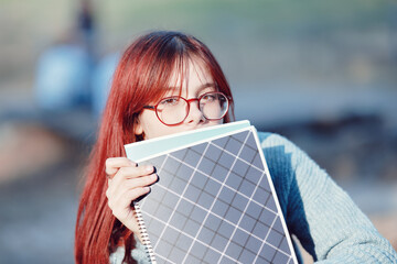 Wall Mural - Red-haired student girl in glasses hides half of her face behind notebooks. Nerd schoolgirl.