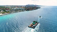 Tug Boat Pulls Barge Along Caribbean Island Coastline At Midday In Beautiful Blue Ocean Water