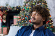 © Liubomir - Close up of a young man with closed eyes resting and breathing fresh air inside the apartment of the house in the living room, for Christmas and New Year, near the tree with gifts, on a winter day.