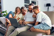 Man sharing laptop with family sitting on sofa at home