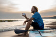 © Westend61 - Young man having coffee sitting on paddleboard at beach