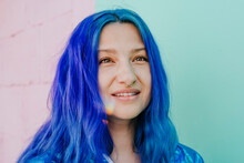 Smiling woman with blue dyed hair in front of wall