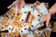 Financial success with hands presenting 50 Euro banknotes above a generous pile, symbolizing wealth, prosperity or financial management, against black backdrop, representation of abundance or opulence
