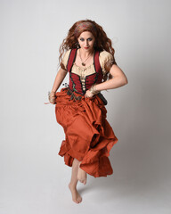 Sticker - Full length portrait of beautiful red haired woman wearing a medieval maiden, fortune teller costume. Standing pose with dancing gestures, twirling skirt. isolated on studio background.