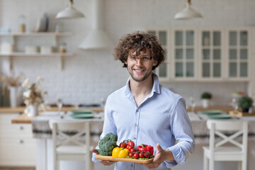 Portrait of a handsome smiling man with vegetables in the kitchen, healthy eating.