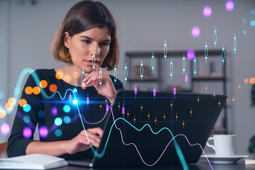 Wall Mural - Pensive attractive beautiful businesswoman in formal wear working on laptop at office workplace in background. Forex graph and charts hologram icons. Concept of market trading and research.