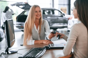 Giving the keys. Female manager is helping woman customer in the car dealership salon