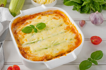 Wall Mural - Delicious zucchini lasagna with sauce bolognese in a baking dish on a white wooden bachground. Healthy food. Top view. Selective focus.