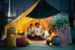 In front of the camera big family two kids and parents enjoy the night time together in the handmade tent sitting down on the floor in the kids room eating popcorn and watching a movie on the laptop