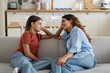 © DimaBerlin - Happy charismatic Italian woman talking with daughter about school friends and summer vacation plans sits on sofa in home interior. Shy casual teen girl shares secrets with mom thanks to family trust
