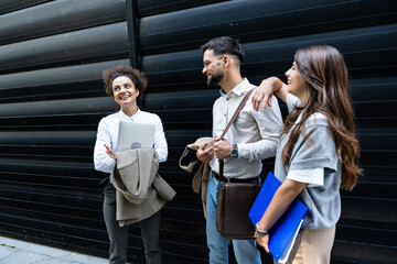 Wall Mural - Group of three young business people experts in marketing telecommuting financial and strategy, talking outside office building. Company workers discussing strategic plans for financial crisis