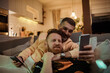 © Marko Geber - Happy gay couple looking at a smartphone on the couch at home