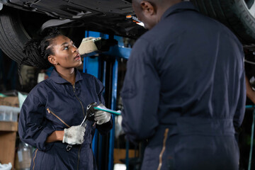 African female mechanic checking and fixing underneath car in automobile repair shop