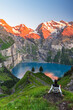© robertharding - View of a hiker resting in front of the Oeschinensee lake surrounded by snowy peak at sunset, Oeschinensee, Kandersteg, Bern Canton, Switzerland