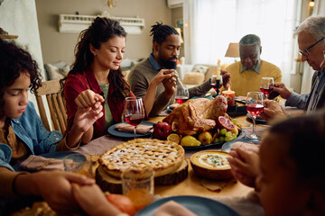 Extended family saying grace while gathering for meal at dining table on Thanksgiving.