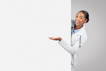 Positive millennial african american lady doctor with big banner point hand at copy space