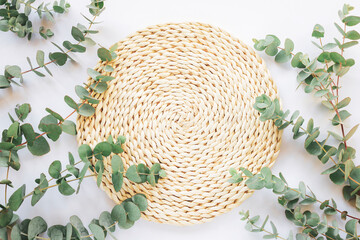 Wall Mural - Wicker place mat with eucalyptus branches on a table. Mockup for cosmetics. Skin care, beauty treatment concept. Top view, flat lay