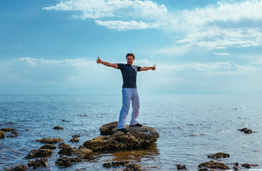 Canvas Print - Handsome successful man standing on rock in the middle of lake and showing thumbs up