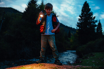 Poster - Boy tourist with flashlight standing in natural park at twilight