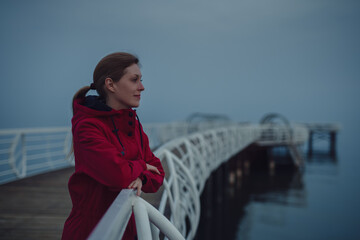 Canvas Print - Young woman tourist standing on the pier and looking at the sea at twilight