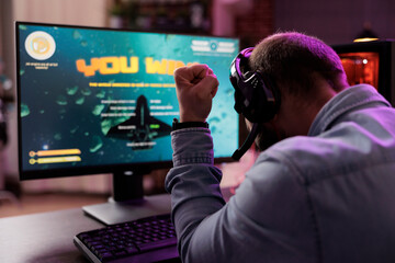gamer playing intense classic arcade spaceship racing videogame, clenching fist in excitement after 
