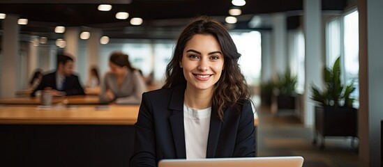Attractive Hispanic woman in office smiling and looking at camera while using laptop