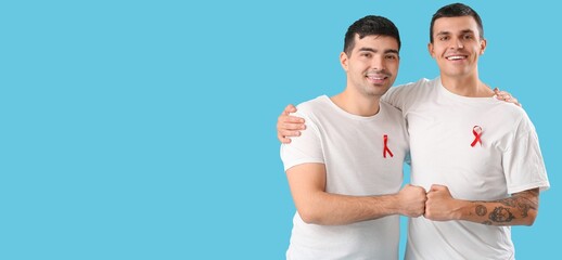 Canvas Print - Young men with red ribbons bumping fists on light blue background with space for text. World AIDS Day