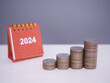 © maybeiii - 2024 desk calendar with stack of coins. The concept of saving money, Financial, Investment and Business growing in new year 2024.