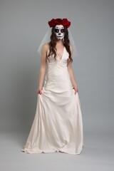 Wall Mural - Young woman in scary bride costume with sugar skull makeup and flower crown on light grey background. Halloween celebration