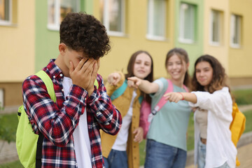 Teen problems. Group of students pointing at upset boy outdoors, selective focus