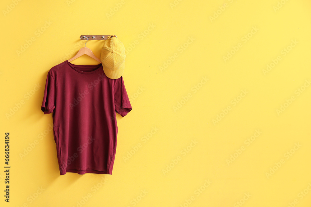 Stylish red t-shirt and cap hanging on yellow background