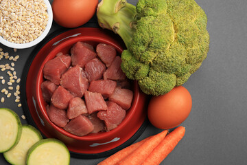 Poster - Raw meat in bowl and healthy products for pet on black background, flat lay