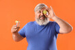 Portrait of senior man with shot of tequila and lime on orange background