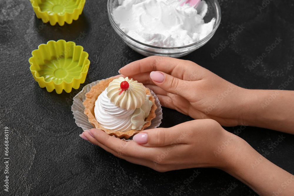Female confectioner with tasty cake on black background